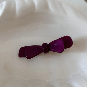 Detail view of a double-layered acetic acid purple bow hair clip on a white shell plate