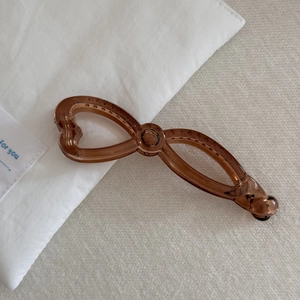 Detail of a brown translucent bow banana hair clip with heart closure on white fabric