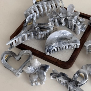 Elegant smokey grey marble acetate hair claws in flower and heart shapes on a wooden tray