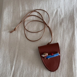 Detail of a brown lychee leather puppy sunglasses holder with Happiness Everyday text