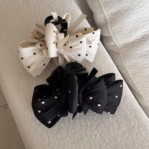 Détail de deux pinces à cheveux à pois en satin noir et crème sur tissu doux