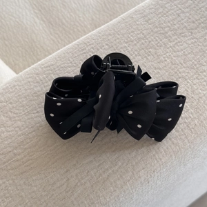 Vue détaillée d'une pince à cheveux en satin noir à pois blancs avec ressort en métal