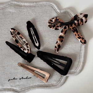 Detail of leopard print hair clips and black velvet clips on a textured linen background