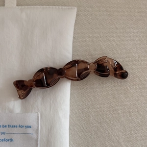 Détail d'une pince à cheveux en résine marron foncé avec texture ambre sur tissu