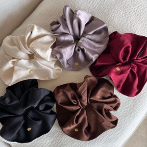 Detail von fünf Premium-Satin-Haargummis mit eleganten Goldlogos und seidiger Textur