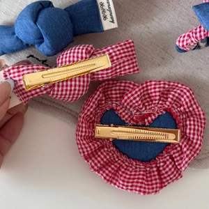 Detailed close-up of handmade denim heart and red plaid bow hair clips with metal grip