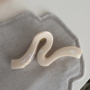 Close-up of wavy cream hair claw clip with white marble texture and gold metal spring