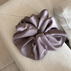 Detail eines Satin-Haargummis in Altrosa mit einem runden Logo-Anhänger aus Goldmetall