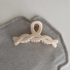 Detail view of the twisted rope design on a glossy cream hair claw clip with gold spring