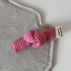 Detail of red gingham fabric knot hair clip featuring a handmade cotton woven label