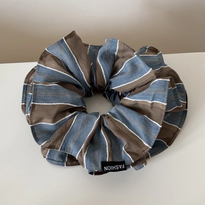 Détail d'un chouchou rayé surdimensionné avec motifs bleu et marron et étiquette en tissu