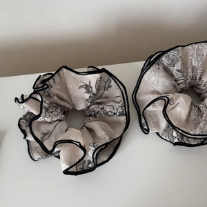 Detailed close-up of two white scrunchies with black floral print and contrast piping