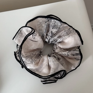 Close-up of beige jacquard scrunchie with black bamboo pattern and stitched edges