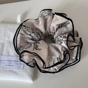 Detail of a large jacquard scrunchie in beige chiffon with black floral patterns and piped edges
