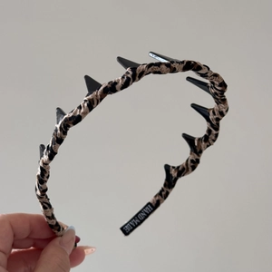Detail of leopard print fabric headband with black spikes and handmade label