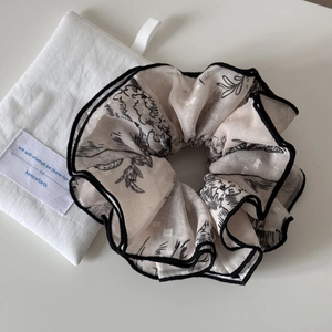 Detailed macro view of large cream jacquard scrunchie with floral prints and black edges