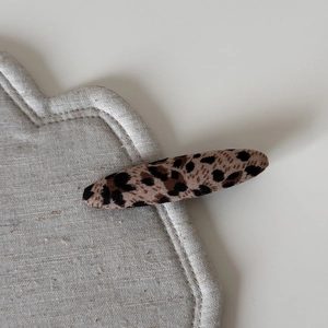 Detail view of large leopard print fabric hair clip on a textured grey background
