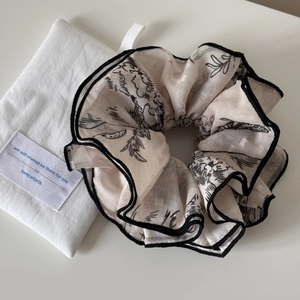Detailed view of beige floral jacquard scrunchie with black piping and storage pouch
