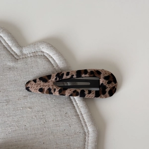 Close-up of leopard print fabric hair clip on soft beige linen cushion background