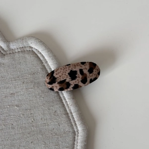 Close-up detail of leopard print fabric hair clip on beige linen textured display pad