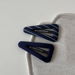 Detailed view of navy blue striped fabric triangle hair clips on a textured mat
