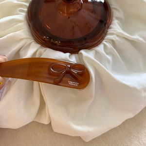Dettaglio del fermaglio per capelli in acetato ambrato con fiocco e logo inciso