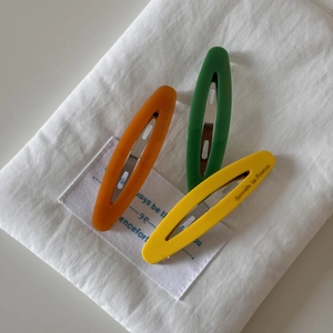 Detailed close-up of three acetate hair clips in orange, green, and yellow with French text