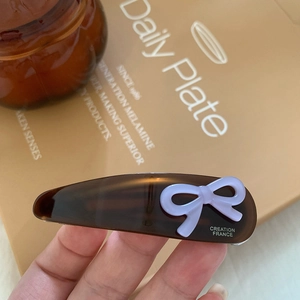 Dettaglio molletta per capelli a goccia in acetato ambrato con fiocco viola e scritte