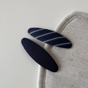 Detail of navy blue striped and solid fabric hair clips on minimalist beige background