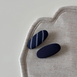 Detail view of navy blue striped and solid twill fabric oval BB hair clips on linen