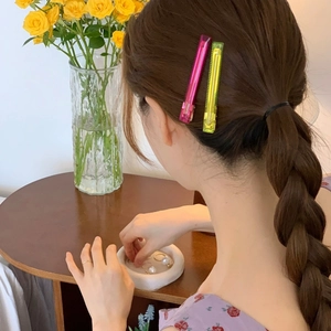 Detail of neon pink and yellow acetate hair clips worn in a stylish side-part hairstyle