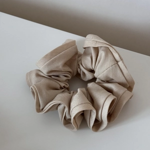 Close-up of beige fabric scrunchie with soft ruffled edge on minimalist white desk