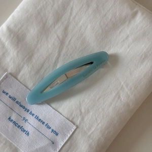 Macro detail of sky blue oval acetate hair clip with silver metal clasp on white fabric