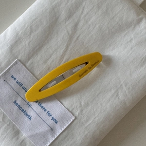 Detail view of a yellow oval acetate French barrette on white fabric background