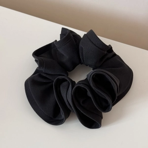 Close-up of black ribbed knit scrunchie with layered fabric textures and soft ruffles