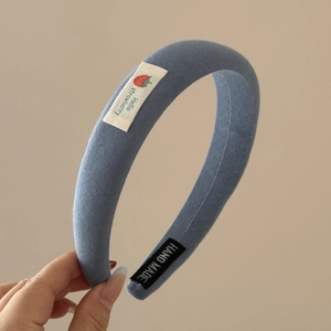 Détail d'un serre-tête en tissu bleu avec une étiquette fraise et une mention fait main