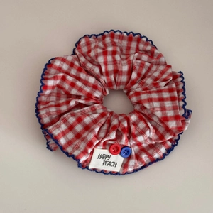 Detail eines rot karierten Scrunchies mit blauem Spitzenrand, Label und bunten Knöpfen