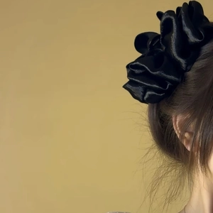 Elegant black pleated fabric flower hair claw clip shown on a soft yellow background