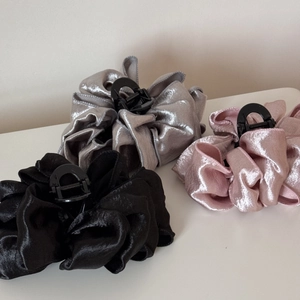 Three large pleated fabric hair claws in black, silver grey and pink displayed on a table