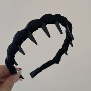 Detail of black wavy shark tooth headband with twisted satin fabric texture and grip combs
