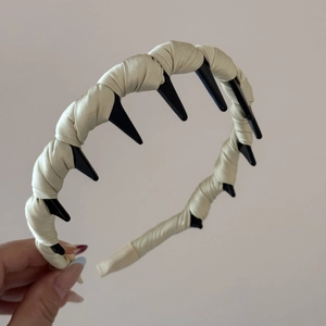 Detail of beige satin padded headband featuring integrated black plastic wavy hair comb teeth