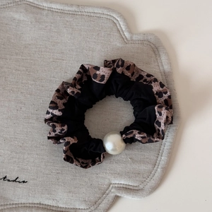 Gros plan d'un chouchou léopard avec une grande perle blanche sur tissu en lin beige