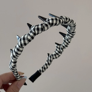Detail showing checkered fabric headband with black punk spikes held by a hand