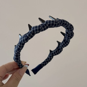 Close-up of blue plaid headband featuring black punk-style decorative spikes