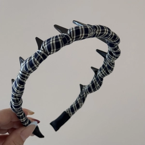 Detail of plaid fabric headband with black punk spikes held against grey wall