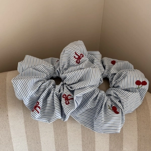 Détail de broderie cerises rouges et nœuds sur un chouchou en tissu à rayures bleues