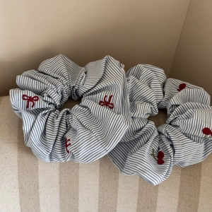 Détail du chouchou en tissu à rayures bleues avec broderie cerise rouge et nœud élégant
