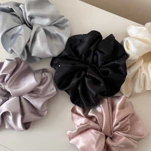 Close-up of assorted satin scrunchies with subtle glitter in silver, lilac, and black