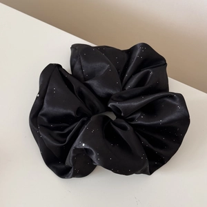 Detailed view of large black satin scrunchie with white polka dots on soft background