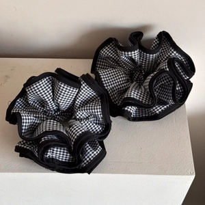 Detail of two black and white gingham scrunchies with ruffles on a white display stand